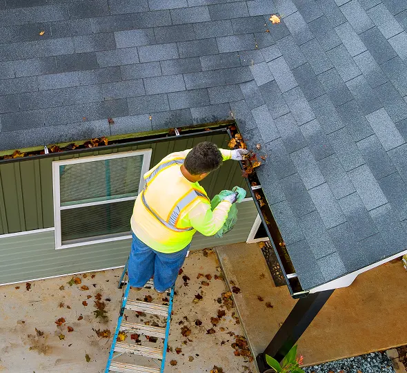 Person maintaining home gutters in autumn